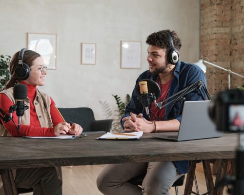 Young man in headphones interviewing a woman at the table during broadcasting at radio studio